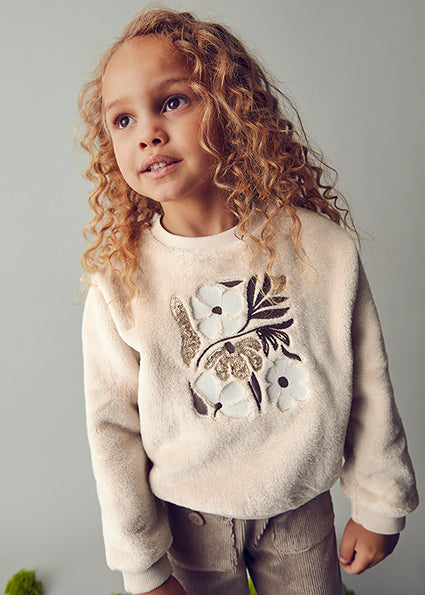 Child wearing a cream sweatshirt with floral design on a gray background